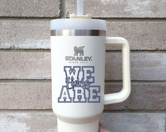 May include: White travel mug with a black handle and a gray logo that says "Stanley Since 1913". The mug has a blue graphic that says "We Lions Are".
