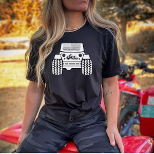 May include: A black t-shirt with a white graphic of a Jeep with an American flag on the hood and mountains in the background.