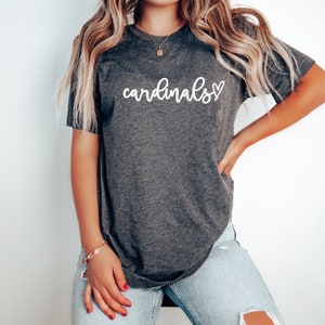 May include: A dark gray t-shirt with the word "cardinals" written in white cursive with a small white heart next to it.
