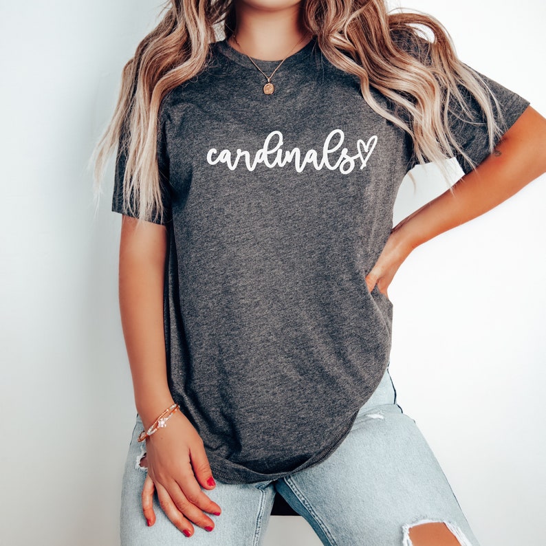May include: A dark gray t-shirt with the word "cardinals" written in white cursive with a small white heart next to it.