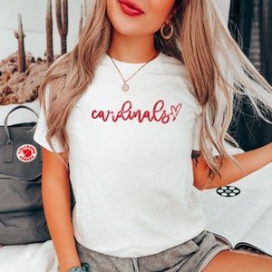 May include: White t-shirt with the text "cardinals" in red script with a red heart next to it.