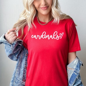May include: Red t-shirt with white cursive text that says "cardinals" with a small heart after the "s".