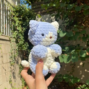 May include: A crocheted plush toy in the shape of a cat. The cat is light blue and white with a fluffy texture.