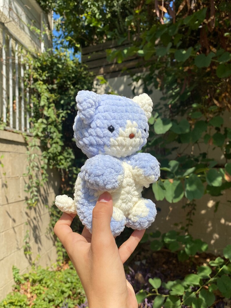 May include: A crocheted plush toy in the shape of a cat. The cat is light blue and white with a fluffy texture.