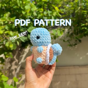 May include: A crocheted blue and tan turtle plushie with a white belly and brown shell. The text "PDF PATTERN" and "low sew!" are visible in the image. The plushie is held in front of a green leafy background.