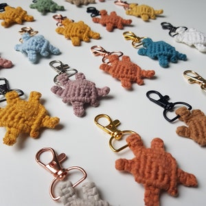 Könnte beinhalten: Eine Sammlung bunter gehäkelter Schildkröten-Schlüsselanhänger mit Metallringen. Die Schildkröten sind aus verschiedenen Farben Garn gefertigt, darunter Gelb, Orange, Rosa, Blau, Grün und Weiß.