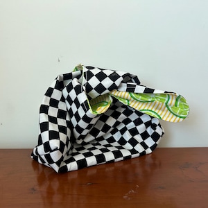 May include: A black and white checkered tote bag with a lime and yellow patterned interior. The bag is made of fabric and sits on a wooden surface. The bag's handles are visible.