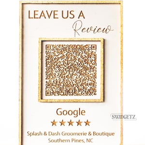 May include: A wooden sign with a QR code and the text "LEAVE US A Review" and "Google" with five stars. The sign also includes the text "Splash & Dash Groomerie & Boutique" and "Southern Pines, NC".