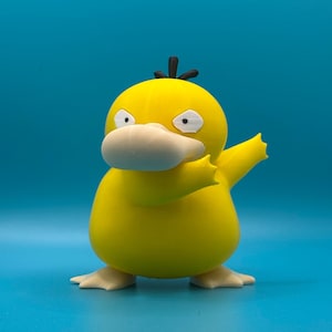 May include: A yellow Psyduck figurine with a white bill and feet, and small black hair tufts. The figure is posed with one arm raised, set against a solid blue background. The figurine is a collectible item.
