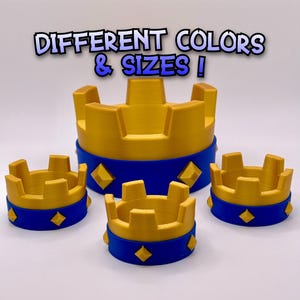 May include: A collection of gold and blue crown-shaped objects. The crowns have a gold top and a blue base with diamond-shaped accents. The text "DIFFERENT COLORS & SIZES !" is displayed above the crowns.