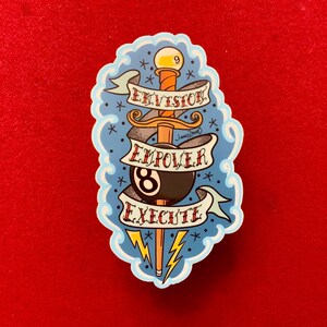 May include: A blue and white sticker with a tattoo-style design. A dagger with a black and white 8-ball on the handle is surrounded by a banner with the words "Envision, Empower, Execute".