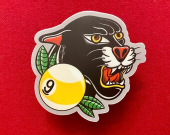 May include: A black panther with a snarling expression, holding a yellow billiard ball with the number 9 on it. The panther is surrounded by green leaves.