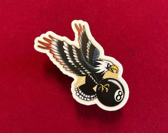 May include: A sticker featuring a cartoon bald eagle with red, white, and blue feathers holding a black and white 8-ball.
