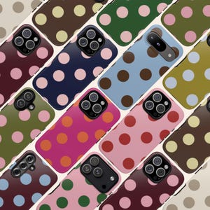 以下が含まれることがあります： さまざまな色のスマートフォンケースのコレクション。それぞれに水玉模様が施されています。ピンク、青、緑、茶色などの色が含まれます。ケースは斜め格子状に配置され、さまざまなデザインが示されています。