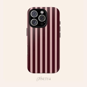 Puede incluir: Funda de teléfono inteligente con un patrón de rayas verticales en burdeos y rosa claro. La funda tiene un acabado brillante y presenta un módulo de cámara con tres lentes. La palabra "NINETY4" está impresa en la parte inferior.