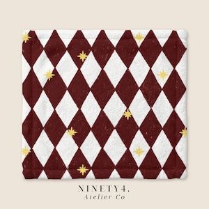Könnte beinhalten: Ein quadratischer Stoffartikel mit einem sich wiederholenden Rautenmuster in Dunkelburgunder und Weiß. Kleine, gelbe vierzackige Sternsymbole sind über die Rauten verteilt. Der Text "NINETY4. Atelier Co" ist unter dem Artikel aufgedruckt.