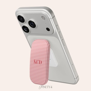 May include: A silver smartphone with a pink and white gingham phone grip. The grip has the initials "KCD" in red. The word "Ninety4" is written in a script font at the bottom.