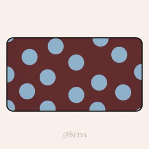 Puede incluir: Un diseño rectangular con un patrón de lunares azul claro sobre un fondo marrón oscuro. El diseño tiene esquinas redondeadas y un borde negro. La palabra "NINETY4" está escrita en cursiva en la parte inferior.