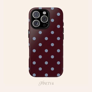 May include: A burgundy phone case with a pattern of light blue polka dots. The case has a glossy finish and a camera module with three lenses. The text "Ninety4" is at the bottom.