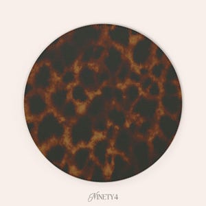 May include: A round coaster with a tortoiseshell pattern in shades of brown and black. The coaster has a stitched black border and the word "Ninety4" in cursive script at the bottom.