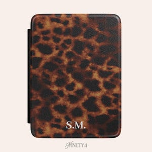 May include: A rectangular case with a brown and black leopard print pattern. The initials "S.M." are in white at the bottom center. The word "Ninety4" is written in cursive at the bottom.