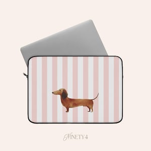 Op de afbeelding: Laptoptas met een roze en wit gestreept patroon en een aquarel illustratie van een teckel. De hoes heeft een zwarte rits en een laptop is gedeeltelijk ingevoegd. De tekst "NINETY4" staat onderaan.