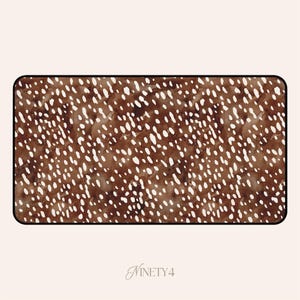 May include: Rectangular desk mat with a brown and white spotted pattern, resembling a deer's coat. The mat has rounded corners and a black border. The text "NINETY4" is in the bottom right corner.