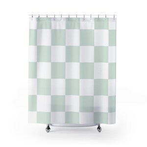 May include: A shower curtain featuring a repeating checkered pattern of alternating light sage green and white squares. The curtain is suspended from a horizontal rod by a series of evenly spaced metal rings along the top edge of the fabric.