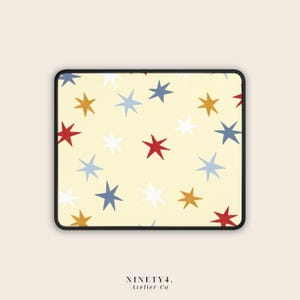 May include: A rectangular mouse pad with a cream-coloured background featuring a repeating pattern of multi-coloured stars in red, gold, light blue, dark blue, and white. The mouse pad has a black stitched border and the text NINETY4. Atelier Co.