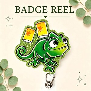 May include: A glittery green chameleon badge reel featuring a cartoon lizard with large eyes and a curled tail. Two yellow lanterns with orange star designs float above the chameleon. The text BADGE REEL is printed in dark green at the top.