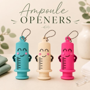 May include: Three ampoule openers in teal, beige, and hot pink, each shaped like a syringe with a smiling face, black measurement markings, and a metal ball chain attached to the top. The text Ampoule OPENERS is printed above the items.