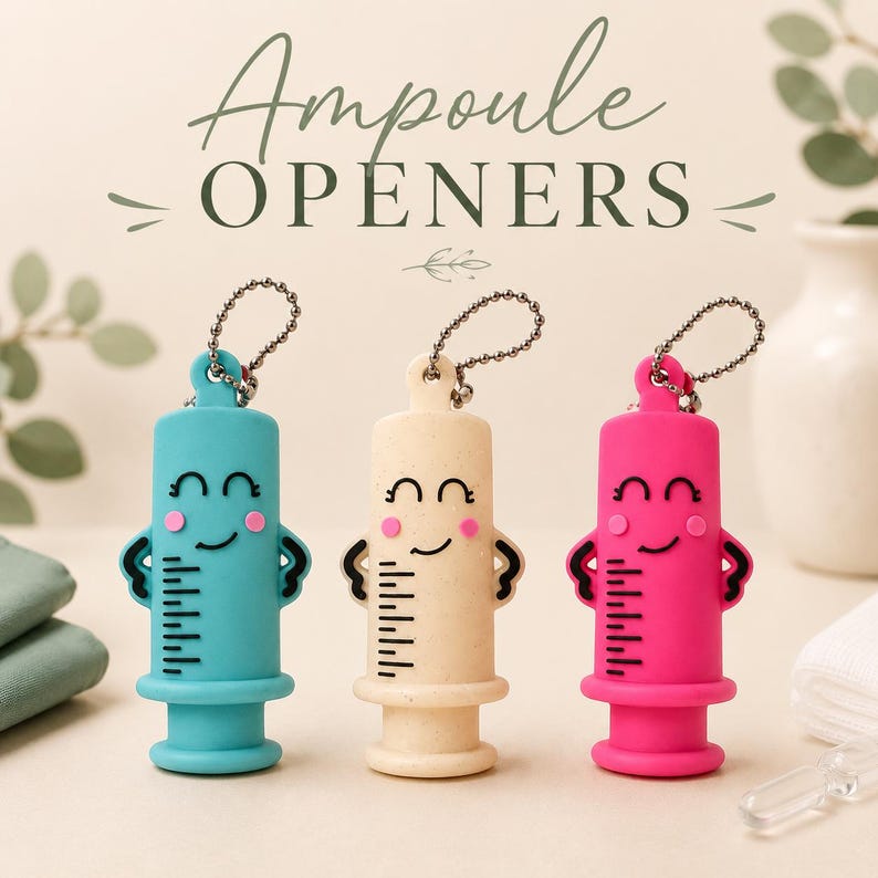 May include: Three ampoule openers in teal, beige, and hot pink, each shaped like a syringe with a smiling face, black measurement markings, and a metal ball chain attached to the top. The text Ampoule OPENERS is printed above the items.
