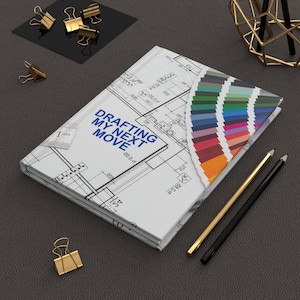 Op de afbeelding: Een wit notitieboek met een blauwdrukontwerp en de tekst "DRAFTING MY NEXT MOVE" is open om een kleurenpalet te onthullen. Gouden en zwarte potloden en paperclips liggen in de buurt.