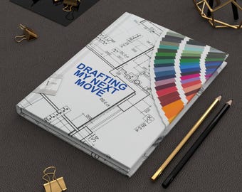 Może przedstawiać: Biały notatnik z projektem planu i tekstem "DRAFTING MY NEXT MOVE" jest otwarty, aby odsłonić paletę kolorów. Złote i czarne ołówki oraz spinacze do papieru znajdują się w pobliżu.