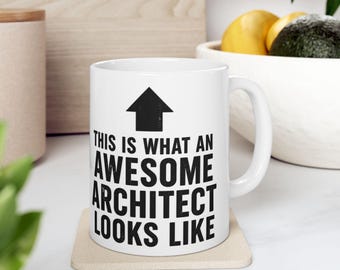 Może przedstawiać: Biały ceramiczny kubek z czarnym napisem "THIS IS WHAT AN AWESOME ARCHITECT LOOKS LIKE" i czarną strzałką skierowaną w górę. Kubek stoi na beżowej podstawce.