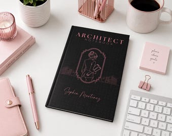 Może przedstawiać: Czarny notatnik architekta z różową ilustracją osoby trzymającej plany. Notatnik zawiera różowy napis "Architect Notebook" i "Sophia Martinez". Inne elementy to różowy długopis, różowy notatnik i klawiatura.