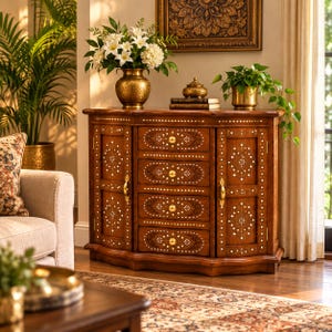 May include: A wooden sideboard featuring four central drawers and two side cabinets, all adorned with intricate white inlay patterns and gold-toned hardware. The piece is topped with a gold vase of white lilies and a small gold decorative box.