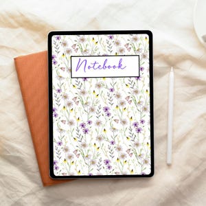 Puede incluir: Una tableta digital con una cubierta de cuaderno floral. La cubierta presenta un fondo blanco con elementos florales morados, amarillos y verdes. La palabra "Notebook" está escrita en cursiva. También se ven un cuaderno naranja y un lápiz óptico blanco.