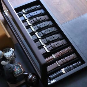 May include: A black watch strap display case with a variety of watch straps in different colours and materials, including leather, fabric, and metal.