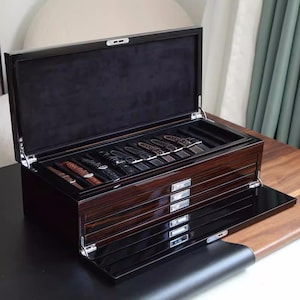 May include: A black wooden watch box with a velvet interior and multiple drawers for storing watches. The box has a sleek, modern design and is perfect for displaying and protecting a collection of watches.