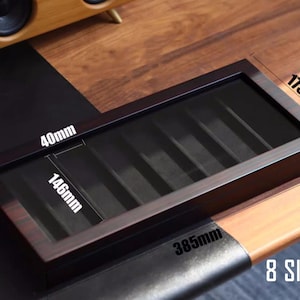 May include: A dark brown wooden box with 8 slots for storing items. The box measures 37 cm long, 10.7 cm wide, and 4 cm tall. The box has a clear plastic lid.
