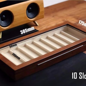 May include: A wooden box with a glass top and 10 slots for storing pens or pencils. The box is 44.5 cm long, 37.1 cm wide, and 10.7 cm deep. The box is made of dark wood and has a light brown interior.