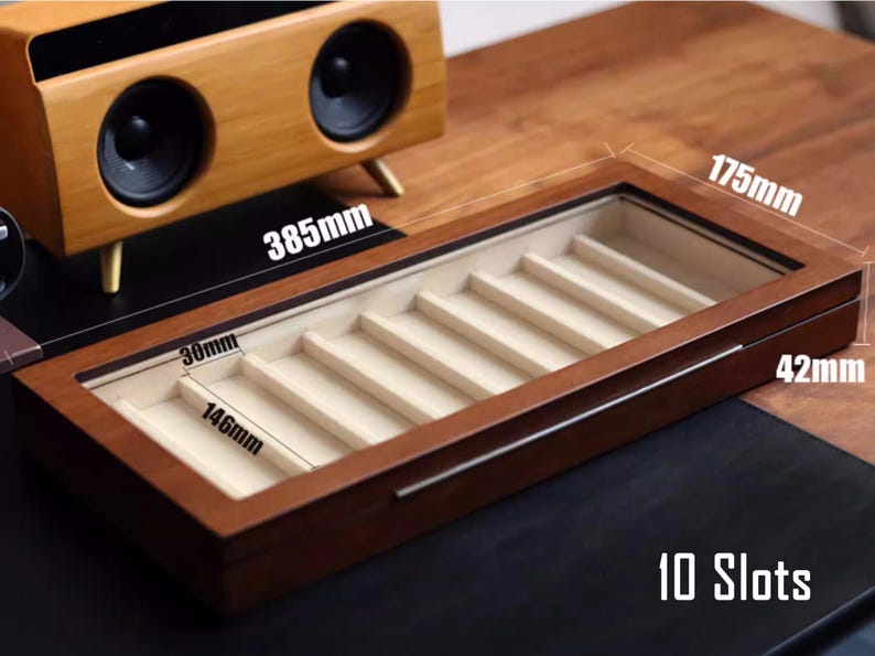 May include: A wooden box with a glass top and 10 slots for storing pens or pencils. The box is 44.5 cm long, 37.1 cm wide, and 10.7 cm deep. The box is made of dark wood and has a light brown interior.