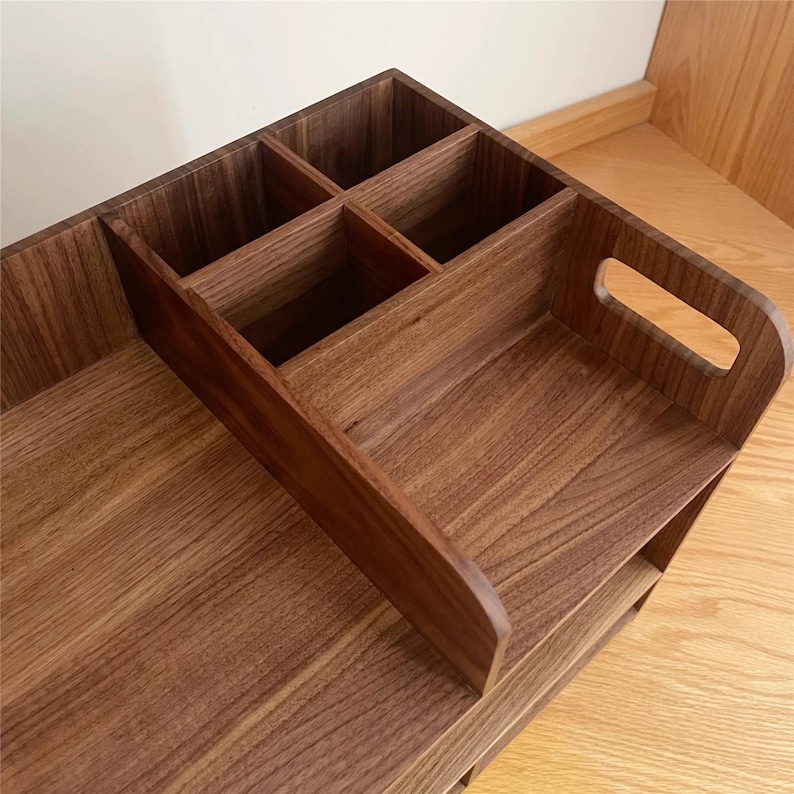 Op de afbeelding: Een houten bureau-organizer in donkerbruin met meerdere compartimenten en een handvat. De organizer is gemaakt van hout en heeft een gladde afwerking. Het heeft verschillende kleine vakken en een groter dienblad, ideaal voor het opbergen van kantoorbenodigdheden.