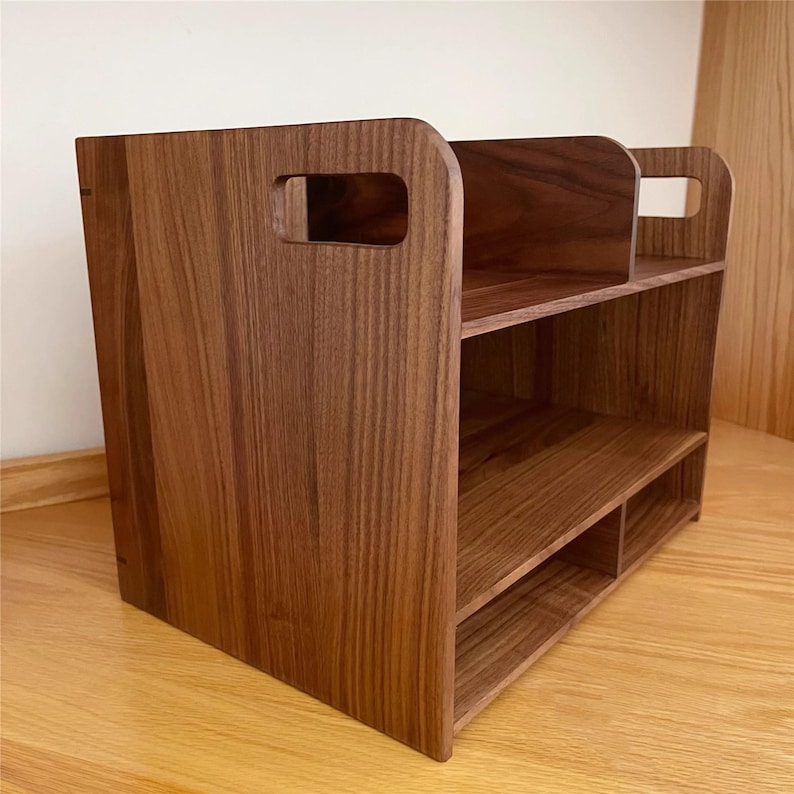 Op de afbeelding: Een houten bureau-organizer met een natuurlijke houtnerf afwerking. De organizer heeft twee planken, een verdeeld onderste gedeelte en een handgreepuitsparing aan elke kant. Het ontwerp is eenvoudig en functioneel.