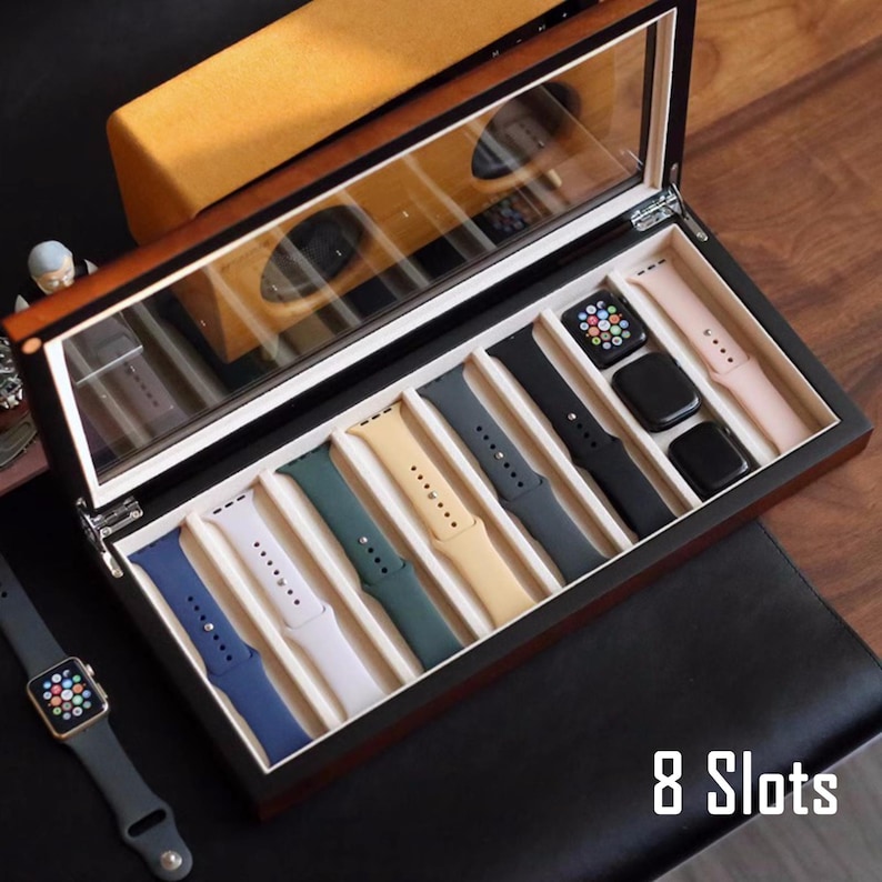May include: A wooden watch box with a clear lid, displaying eight slots for storing Apple Watch bands. The bands are in various colours, including black, white, green, and blue. The box has a dark wood finish and is labelled "8 Slots".