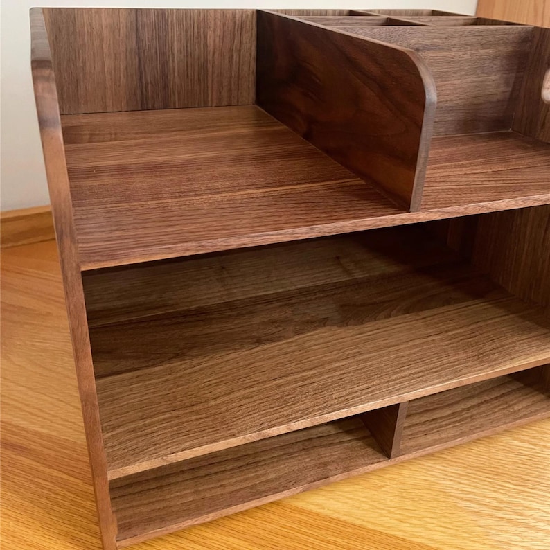 Op de afbeelding: Een houten bureau-organizer met meerdere planken en compartimenten. De organizer is gemaakt van een donkerbruin hout met een natuurlijk nerfpatroon. Het heeft een gelaagd ontwerp met open planken en een bovenste gedeelte met verdelers.