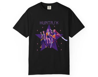 May include: Black t-shirt with a graphic of three stylized figures in front of a purple star. The text "HUNTR/X" is above the figures. Small pink stars are scattered around the design. The t-shirt is made of a soft material.