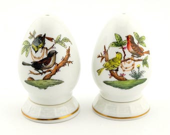 May include: Two white, egg-shaped ceramic salt and pepper shakers. Each shaker features a detailed illustration of colorful birds perched on branches with green leaves. The bases are white with a gold trim.