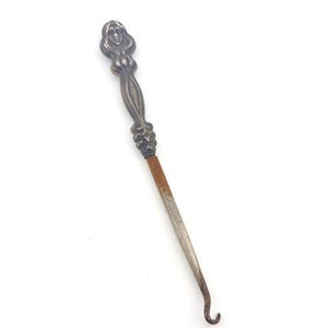 May include: An antique silver-toned letter opener with a detailed figure of a woman at the handle. The blade is a rusty silver color and curves at the end. The opener is set against a white background.